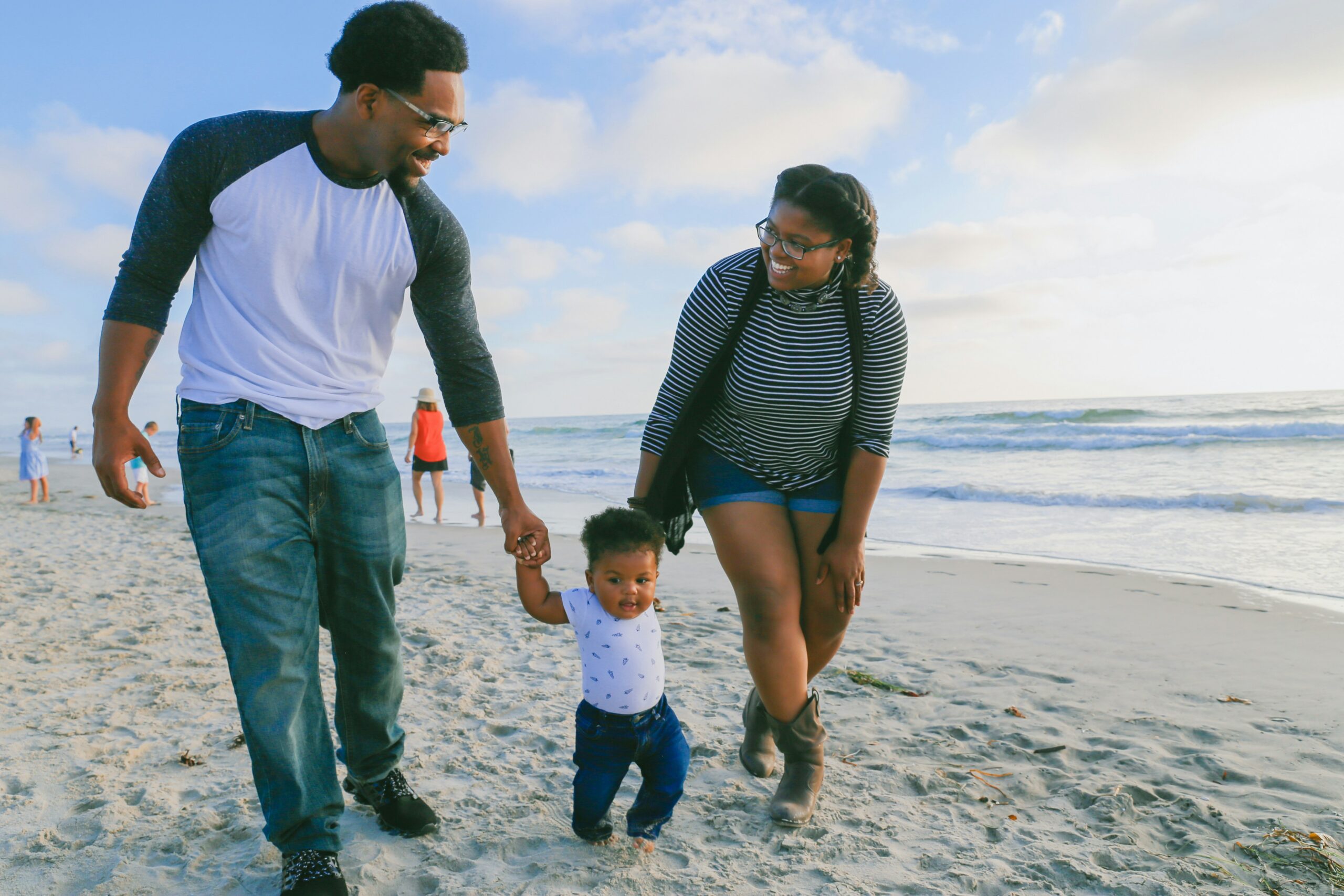 A man and woman walking on a beach holding a baby's hands
